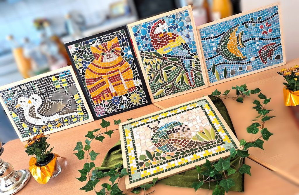 Bunte Mosaikbilder mit Tiermotiven wie Papagei, Katze, Schnecke und Vögeln, ausgestellt in Holzrahmen.