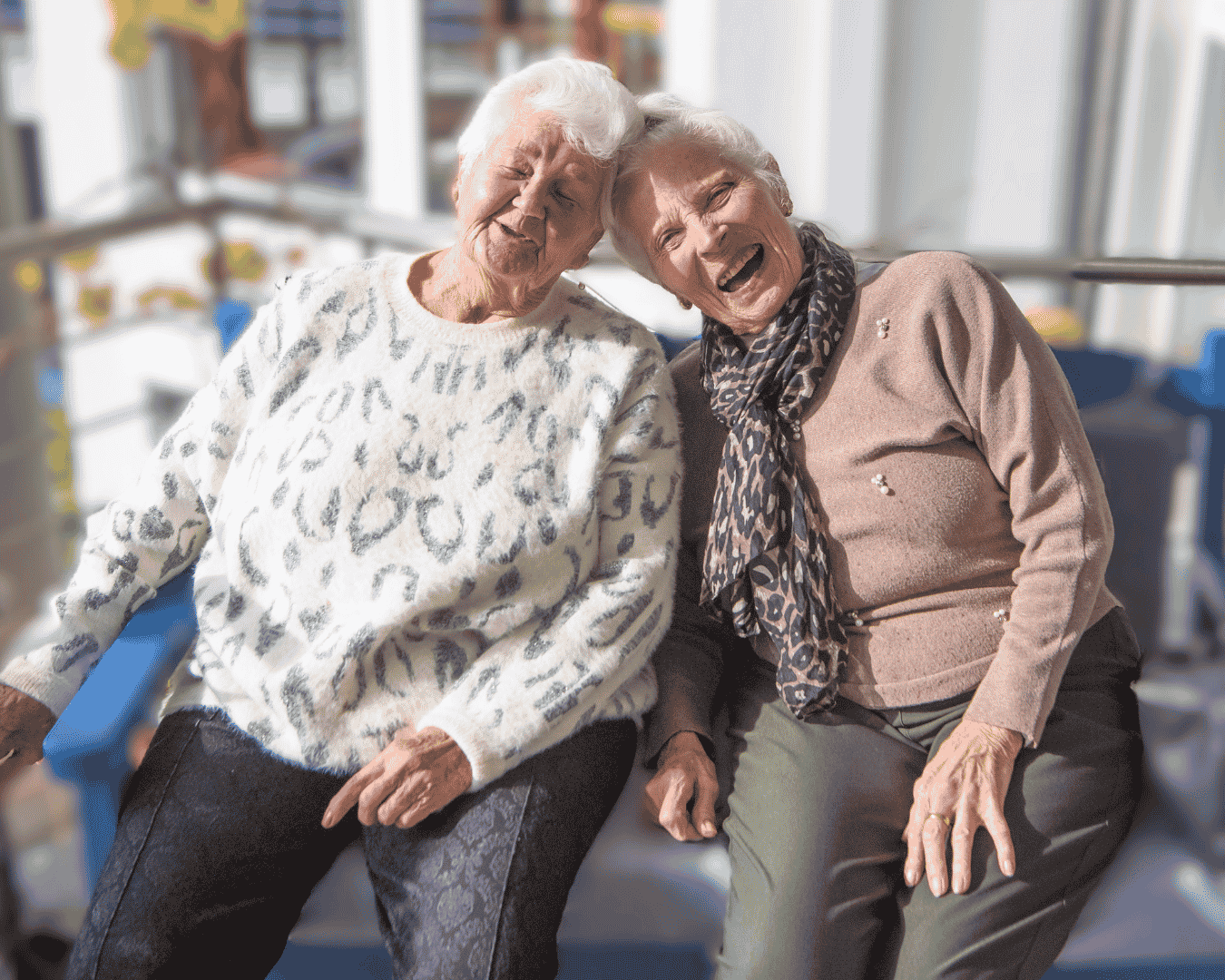 Zwei ältere Frauen sitzen gemeinsam an einem Tisch und lachen fröhlich. Die Szene vermittelt Freude, Gemeinschaft und Geselligkeit in der Tagespflege.