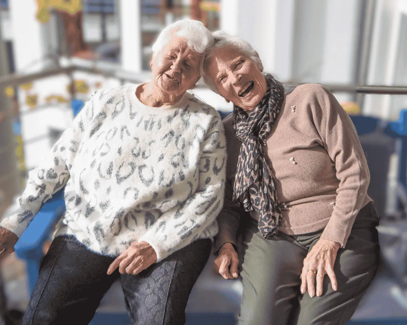 Zwei ältere Frauen sitzen gemeinsam an einem Tisch und lachen fröhlich. Die Szene vermittelt Freude, Gemeinschaft und Geselligkeit in der Tagespflege.