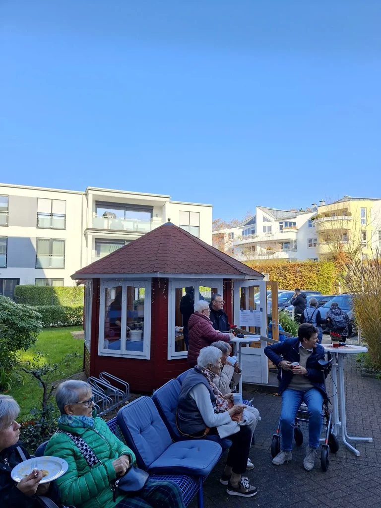 mehrere Personen draußen sitzend vor einem Pavillon