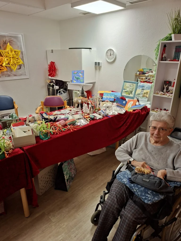 Bewohnerin lacht in die Kamera, im Hintergrund ein Tisch mit verschiedenen Weihnachtsartikeln